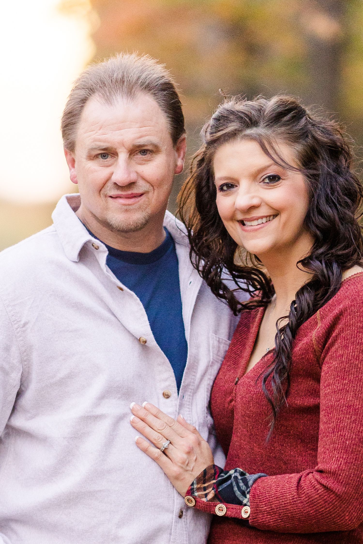 Close up portrait of couple in contrasting sweaters with autumn colors behind them.