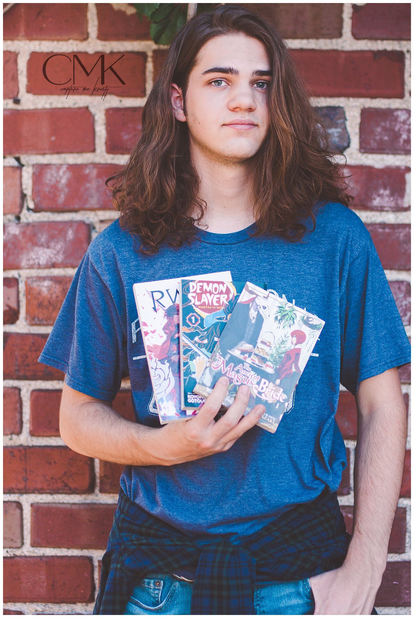 Person in blue shirt holding manga books against brick wall background.