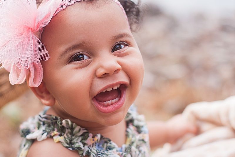 Happy laughing baby in pink headband and floral dress against soft background.