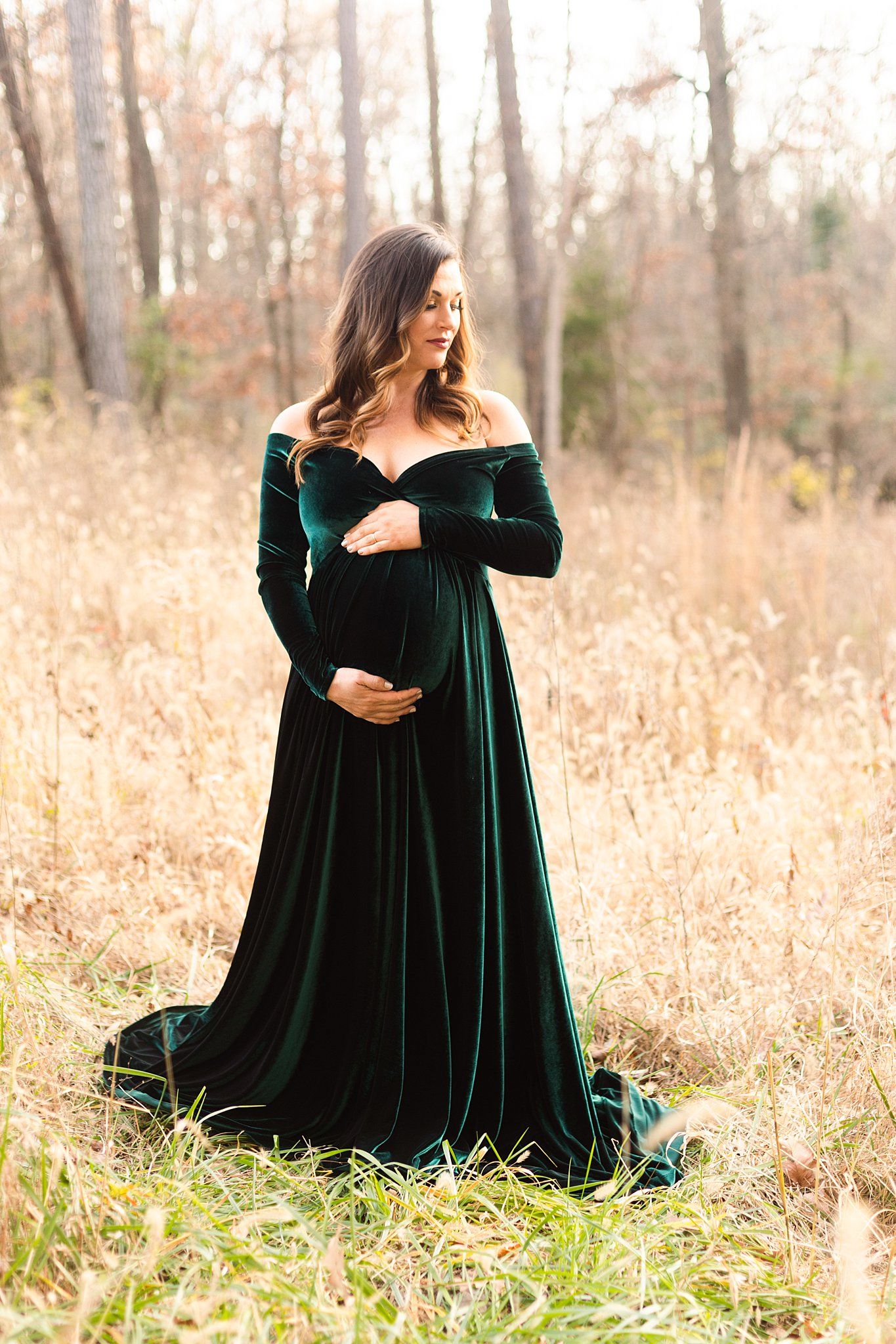 Elegant off-shoulder emerald velvet maternity dress showcased in a golden autumn field setting.