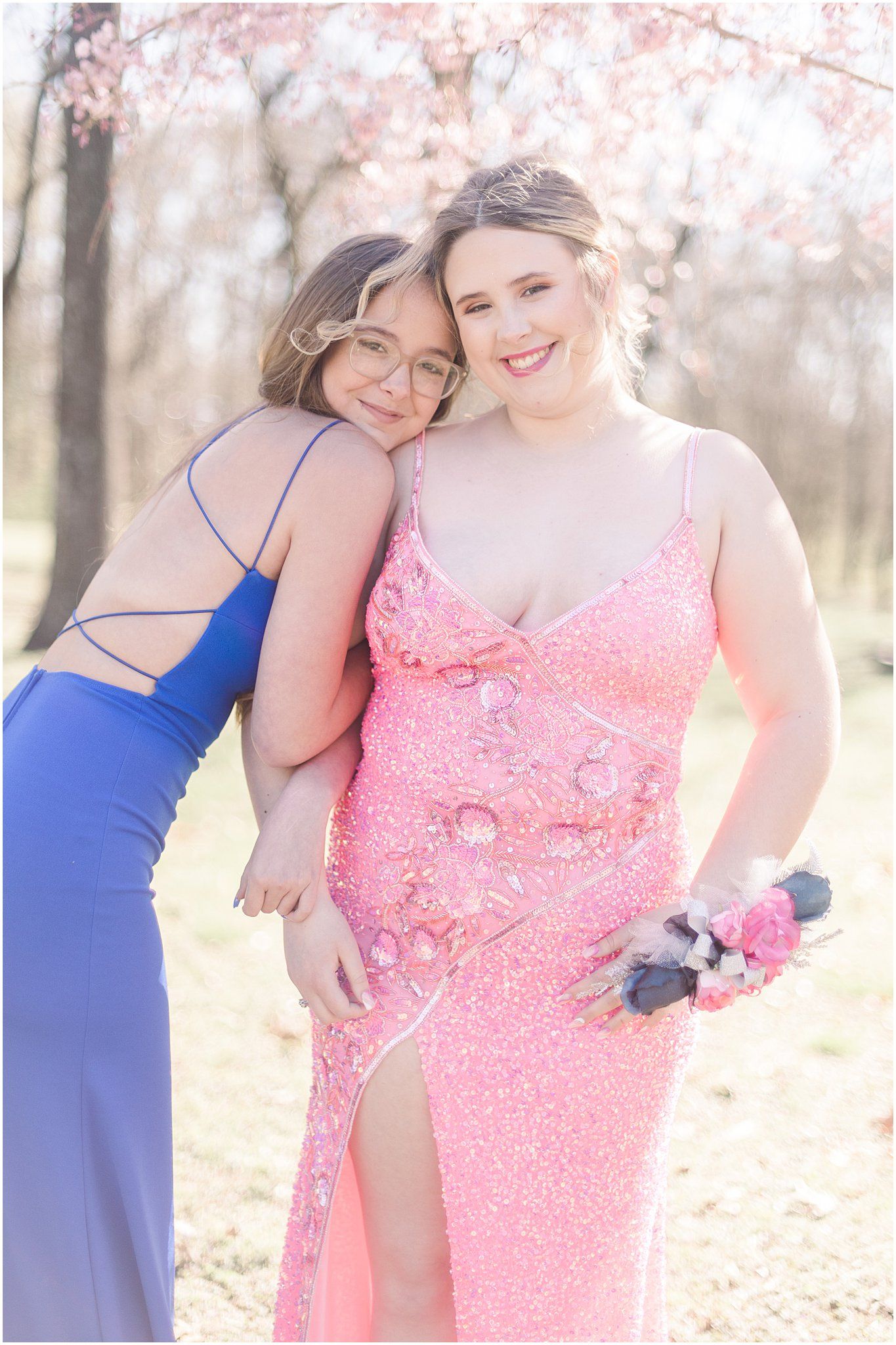 Two friends in formal attire share joyful moment under blooming cherry trees.