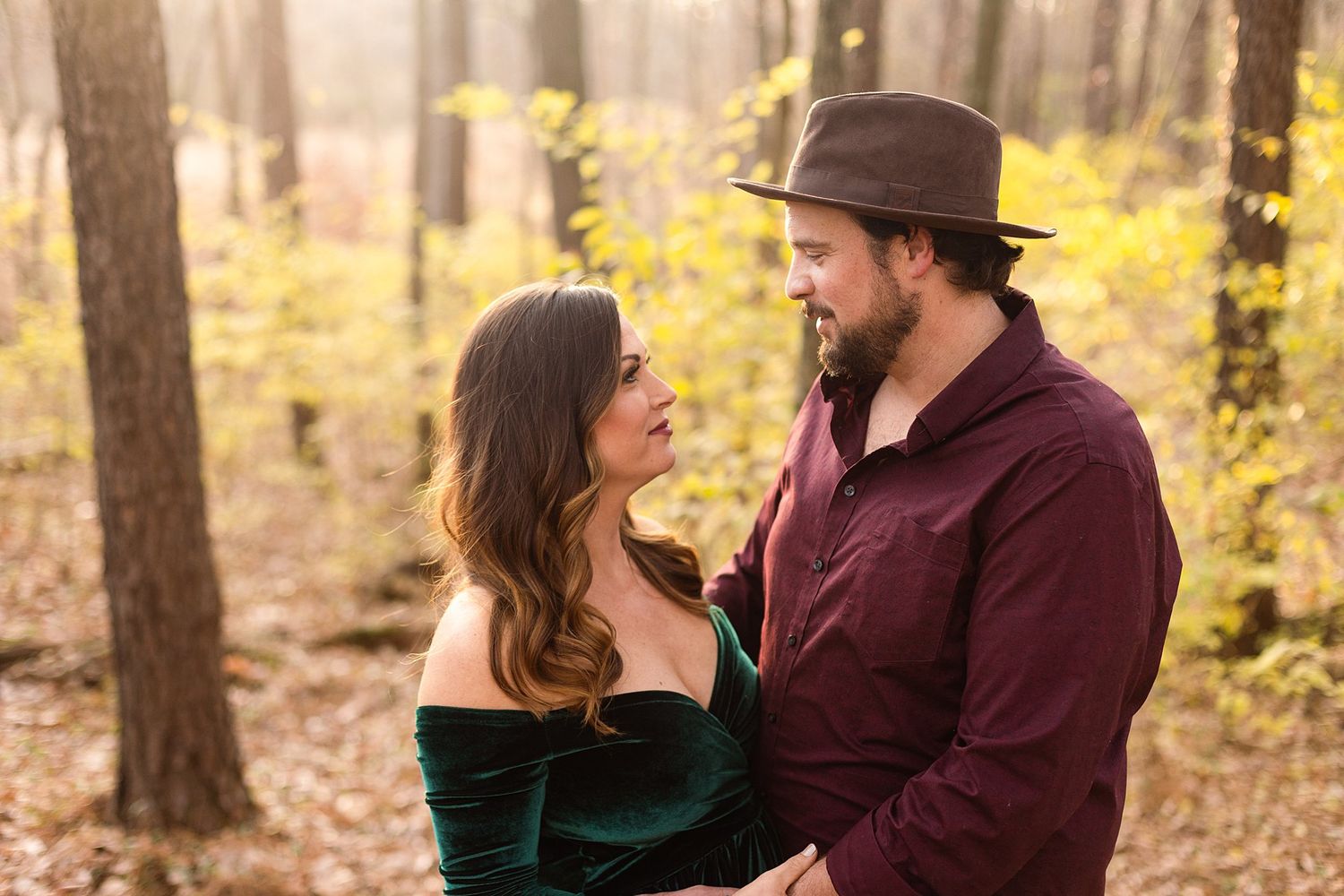 Intimate forest maternity portrait with couple in burgundy and emerald velvet.