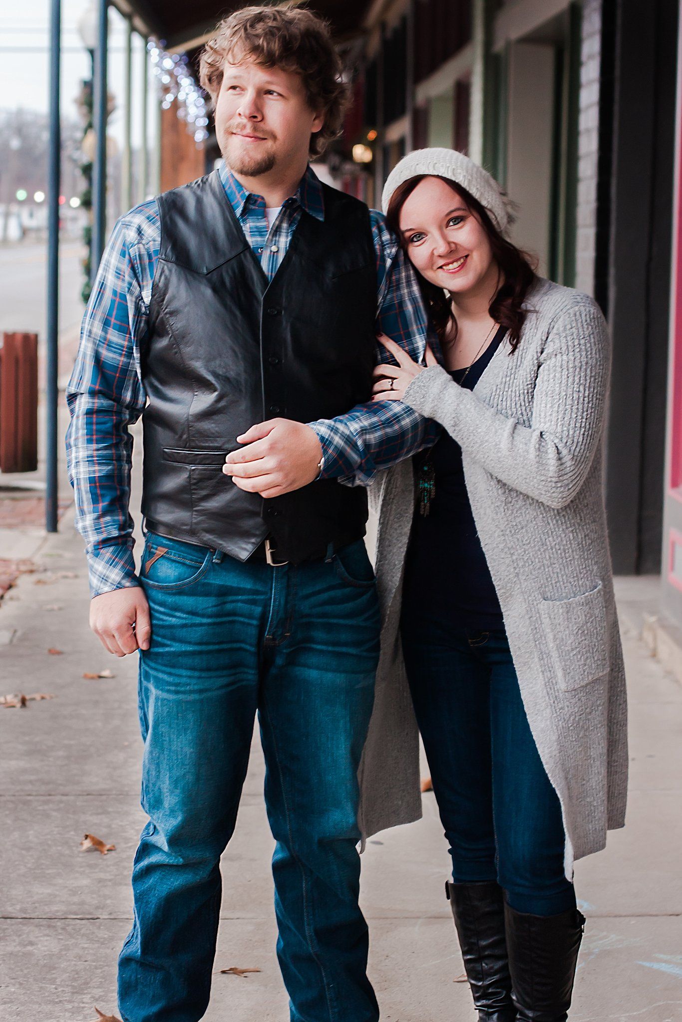 Woman leans and holds arm of fiancé as he looks off camera