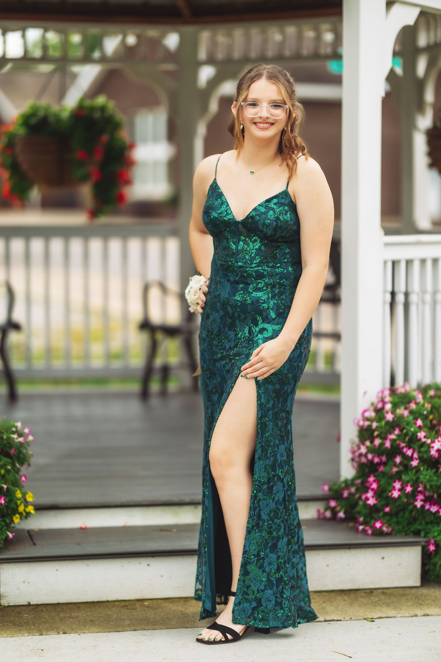 Emerald green velvet formal dress photographed on a white gazebo porch with pink flowers.