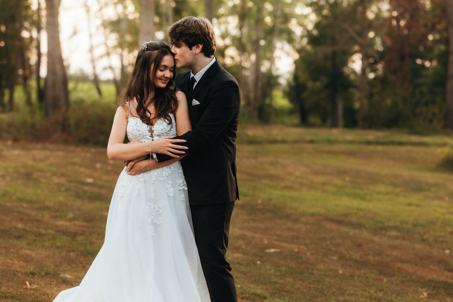 Intimate wedding portrait of newlyweds embracing in a golden-lit forest setting.