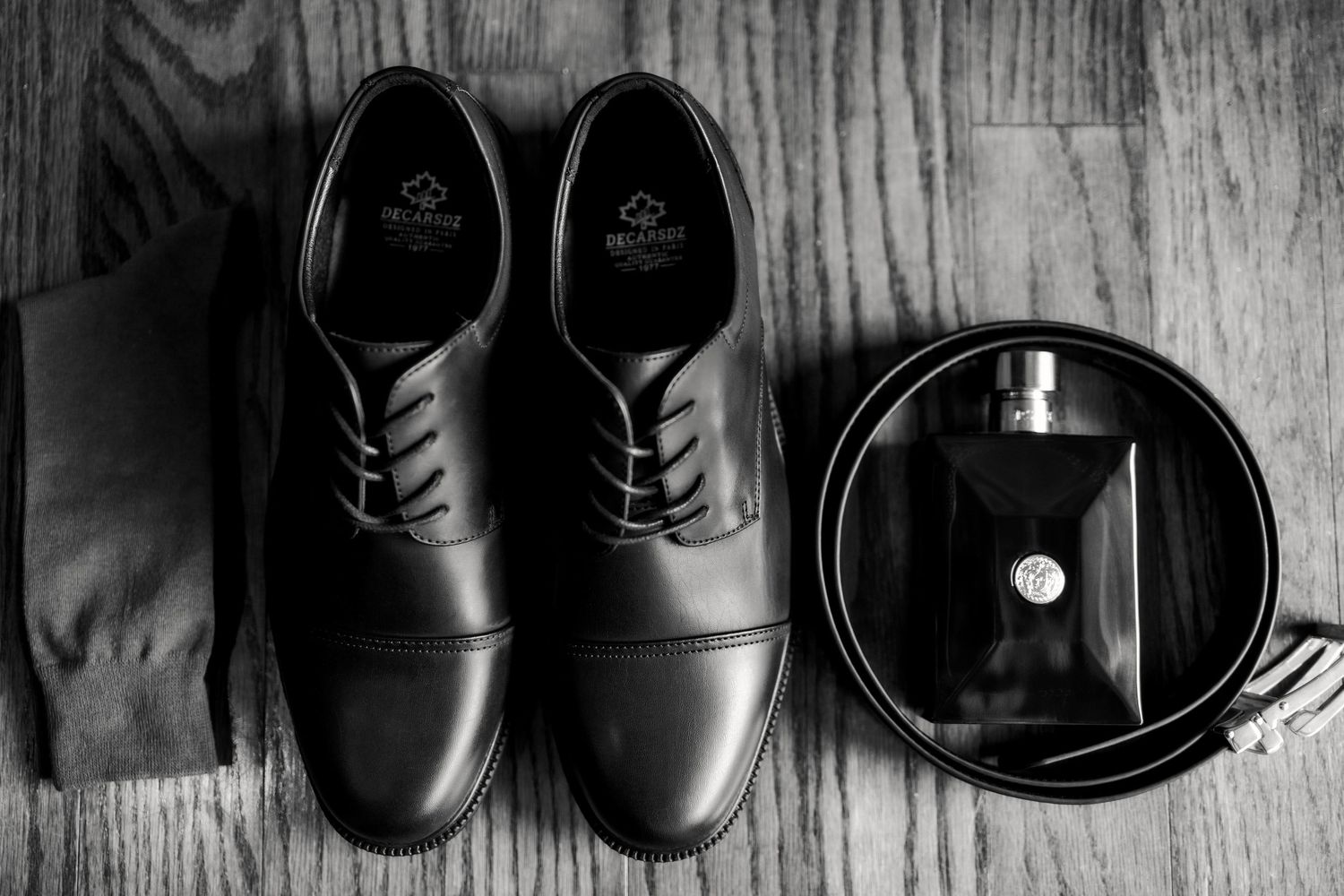Black and white image of formal men's dress shoes arranged on wooden floor.