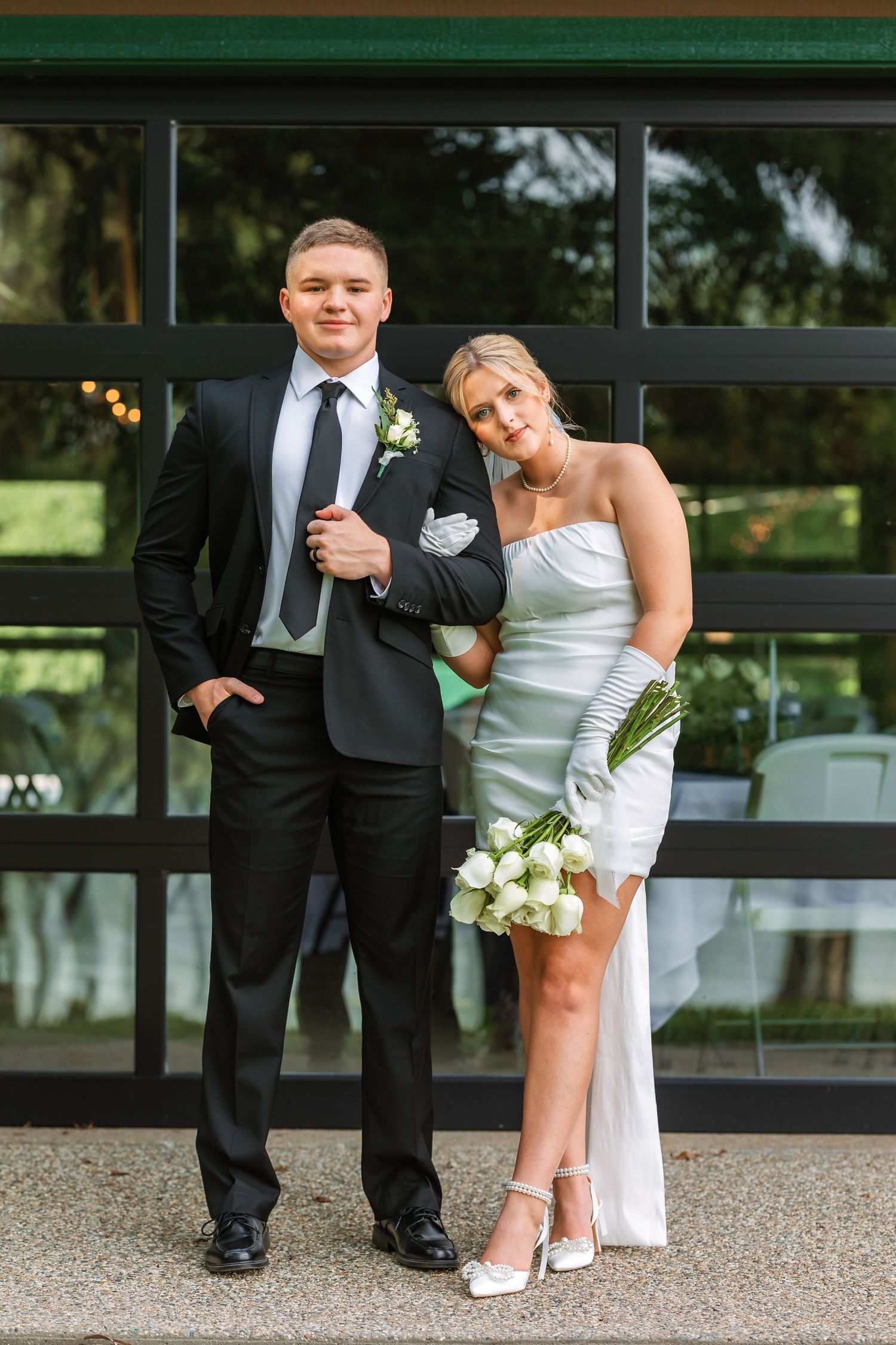 Playful wedding couple posing together near a modern building exterior.