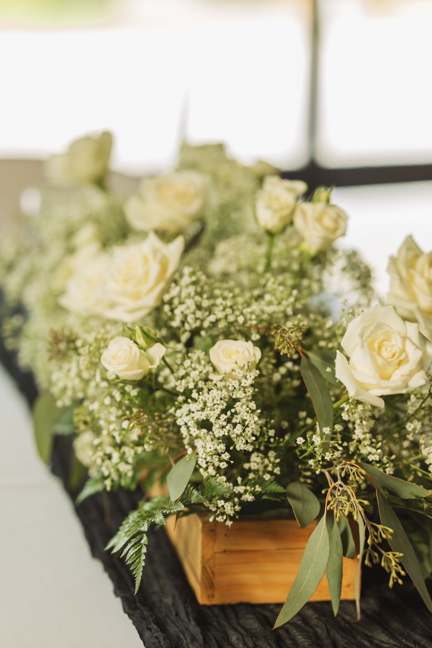 Elegant white roses and baby's breath arranged in wooden boxes with eucalyptus leaves for wedding decor.