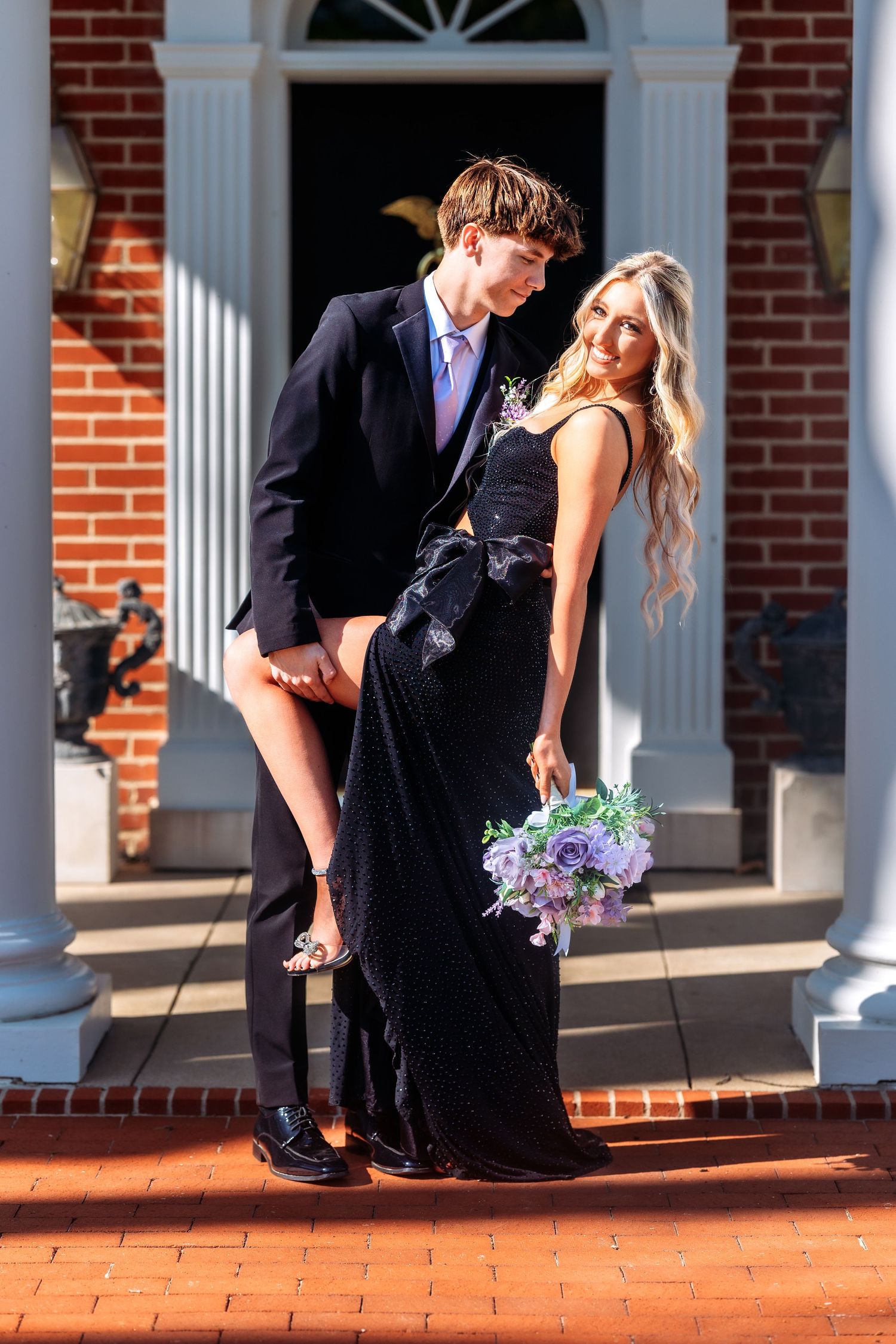A couple in formal attire dances elegantly on a brick patio in front of a white-columned brick building.