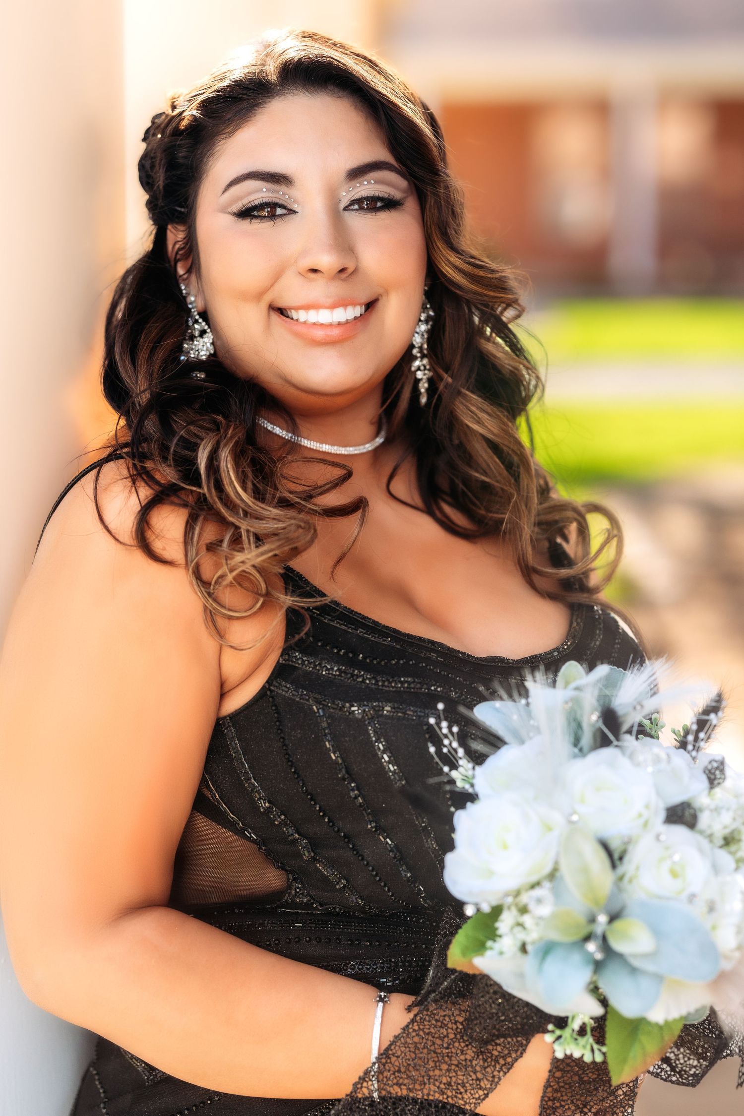 A person in a black sequined formal dress poses with a white floral bouquet in an outdoor setting.