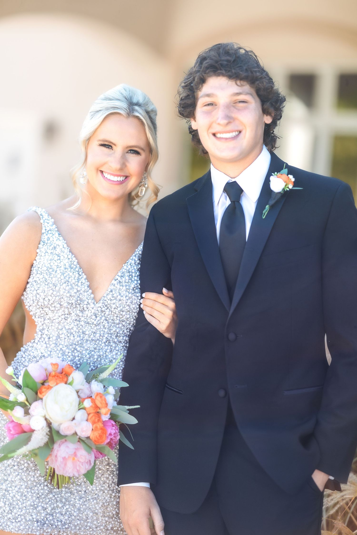 Formal couple in navy suit and floral dress pose together with bouquet.
