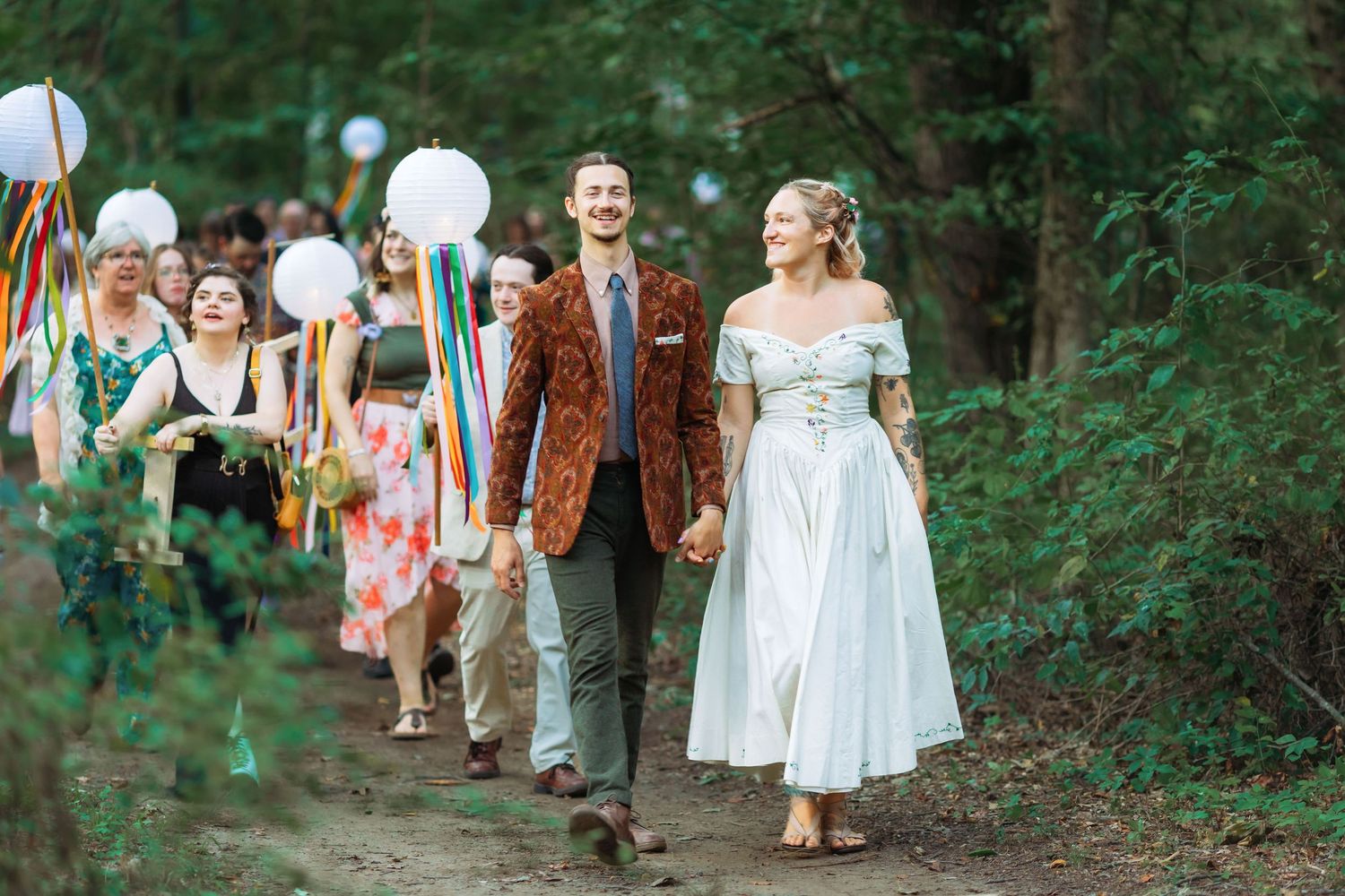 Celebratory procession through forest path with white balloons and colorful attire.