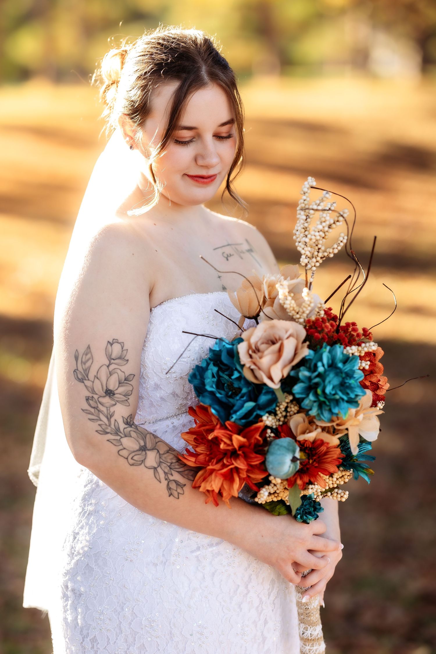 Wedding bouquet featuring vibrant teal and burnt orange flowers held against a white lace dress in autumn sunlight.