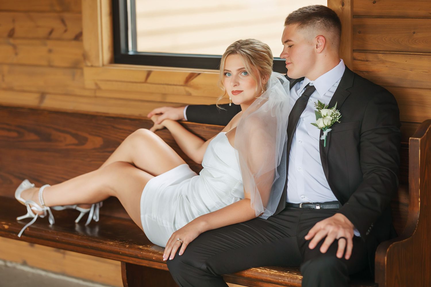 Wedding couple sharing intimate moments on wooden bench in rustic setting.