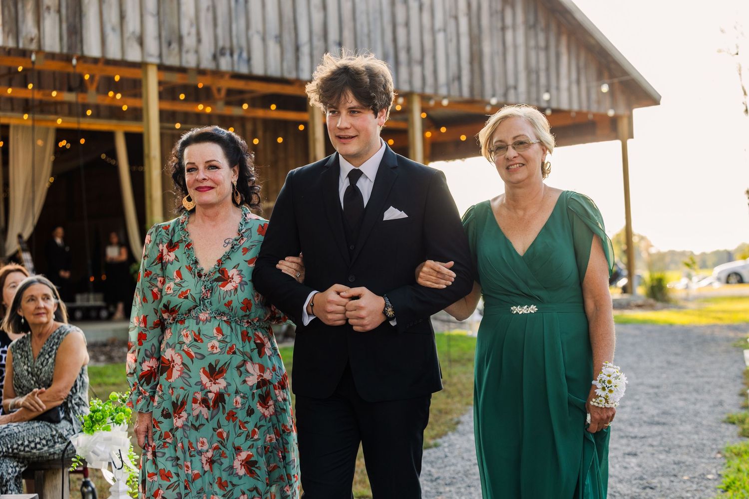 Wedding party members walk together outside a rustic barn venue.