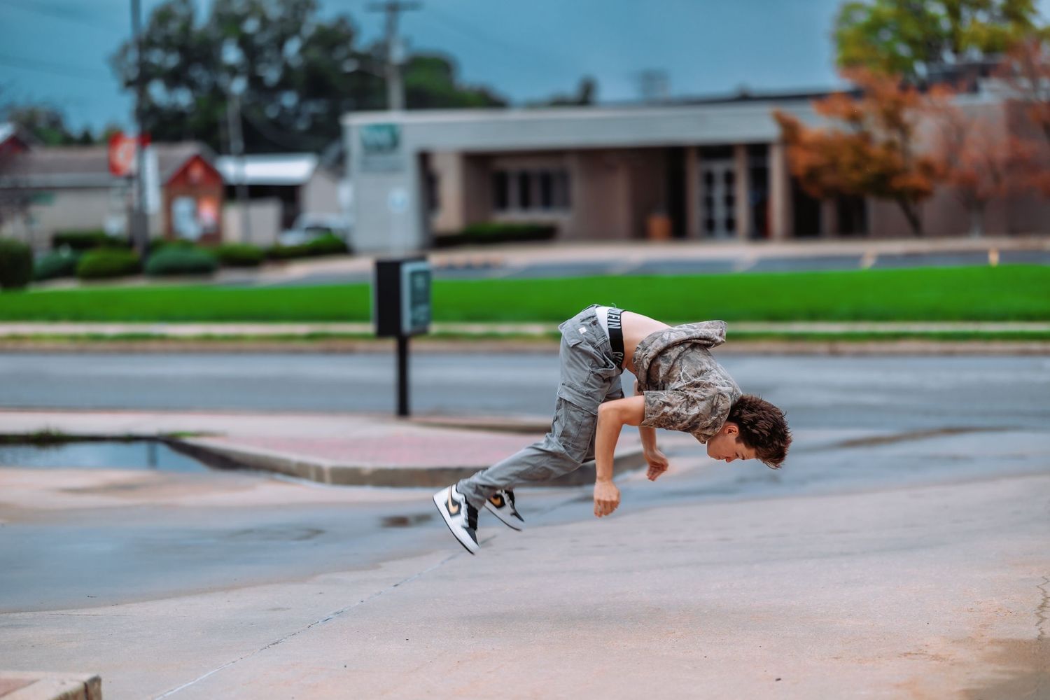 A skateboarder performs a dynamic trick in mid-air at a skate park with buildings visible in the background.