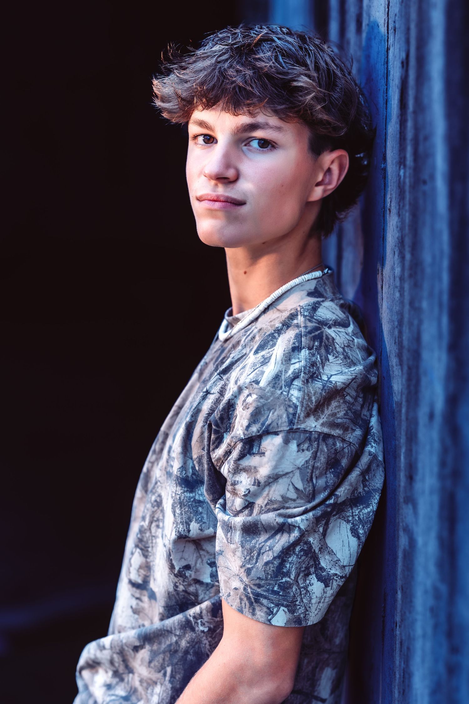 A person in a gray camouflage t-shirt poses against a dark blue background in a photo series.