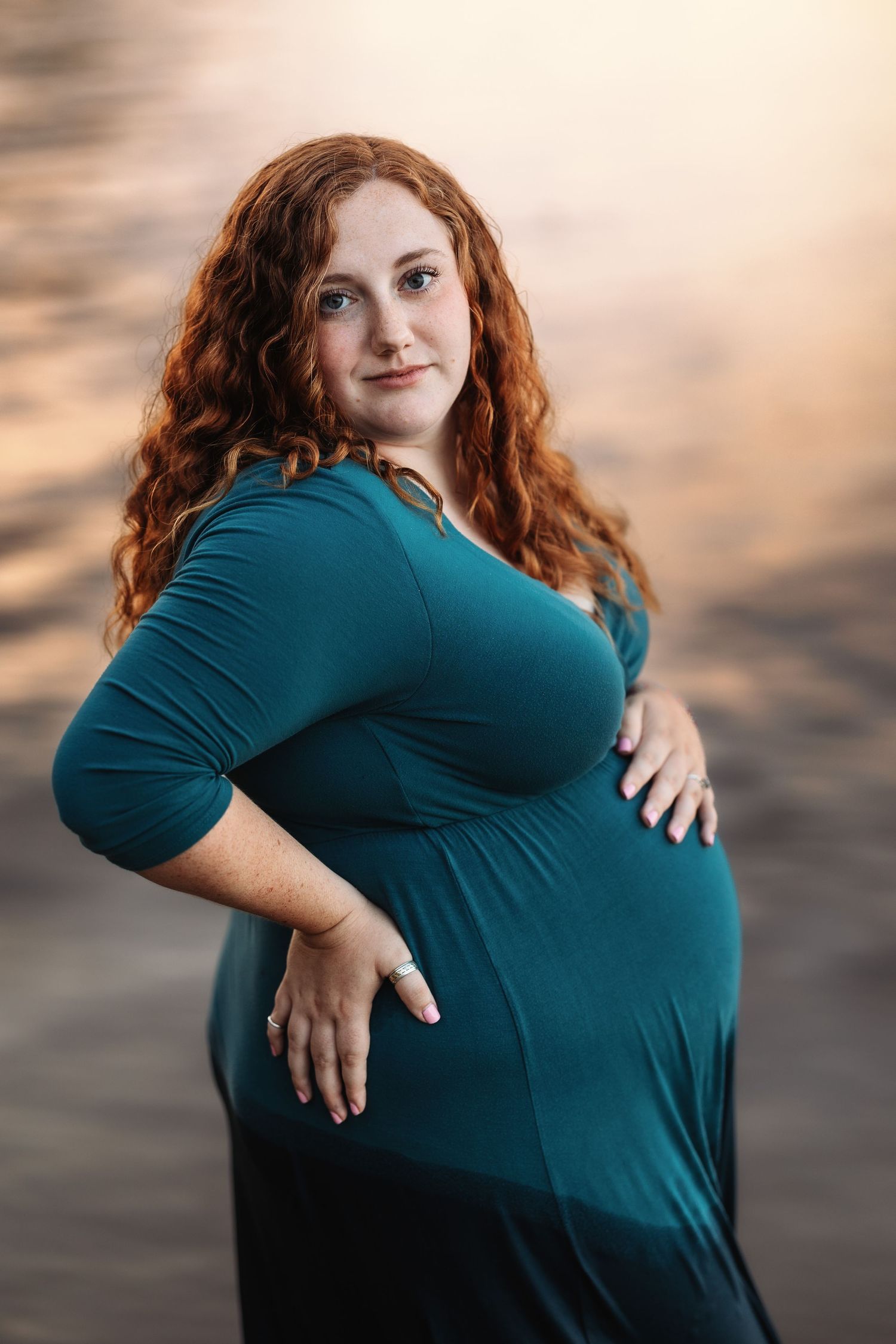 A person in a teal dress poses expressively during a sunset photo session.