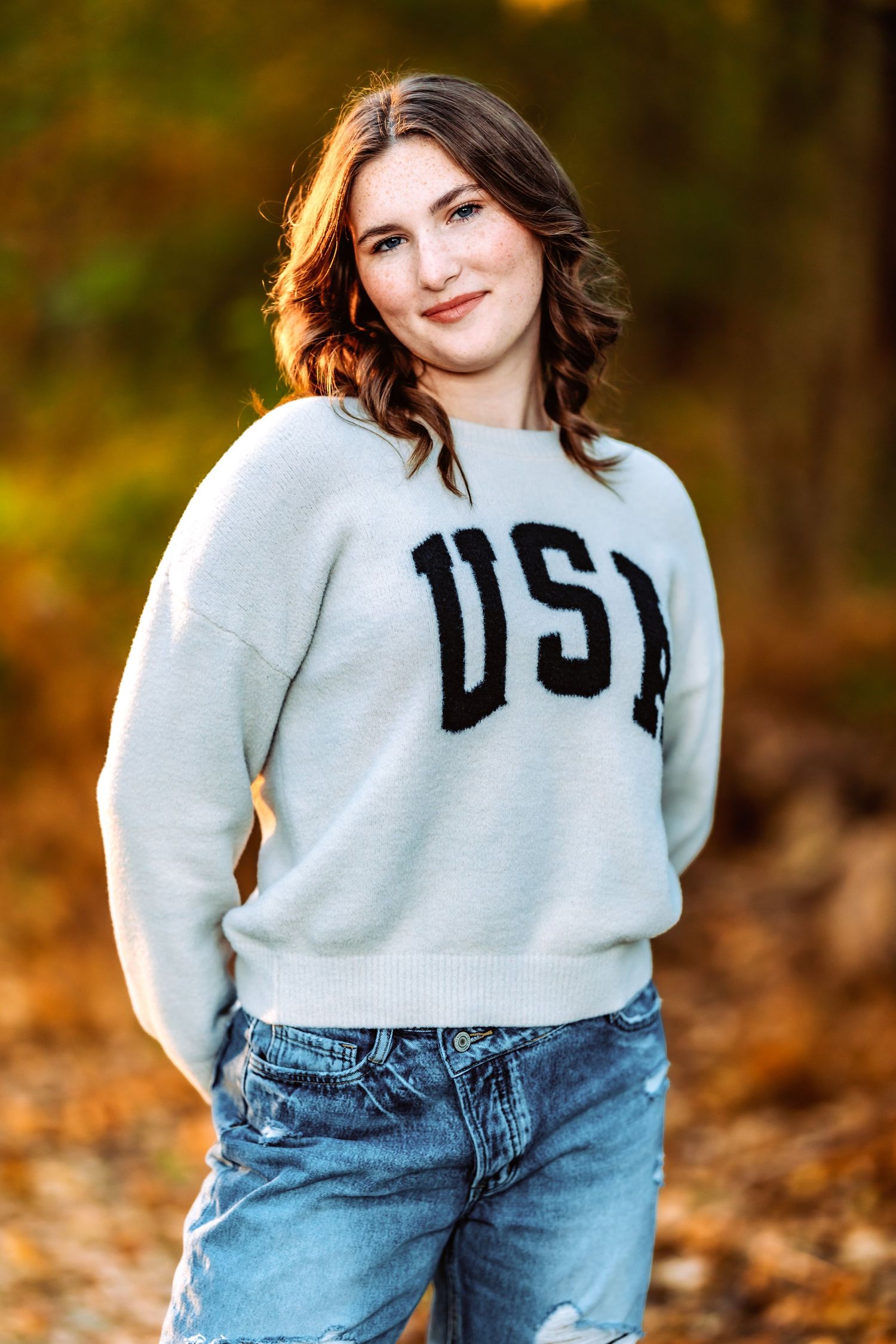 Casual autumn portrait session featuring a USA sweatshirt and jeans among fallen leaves.