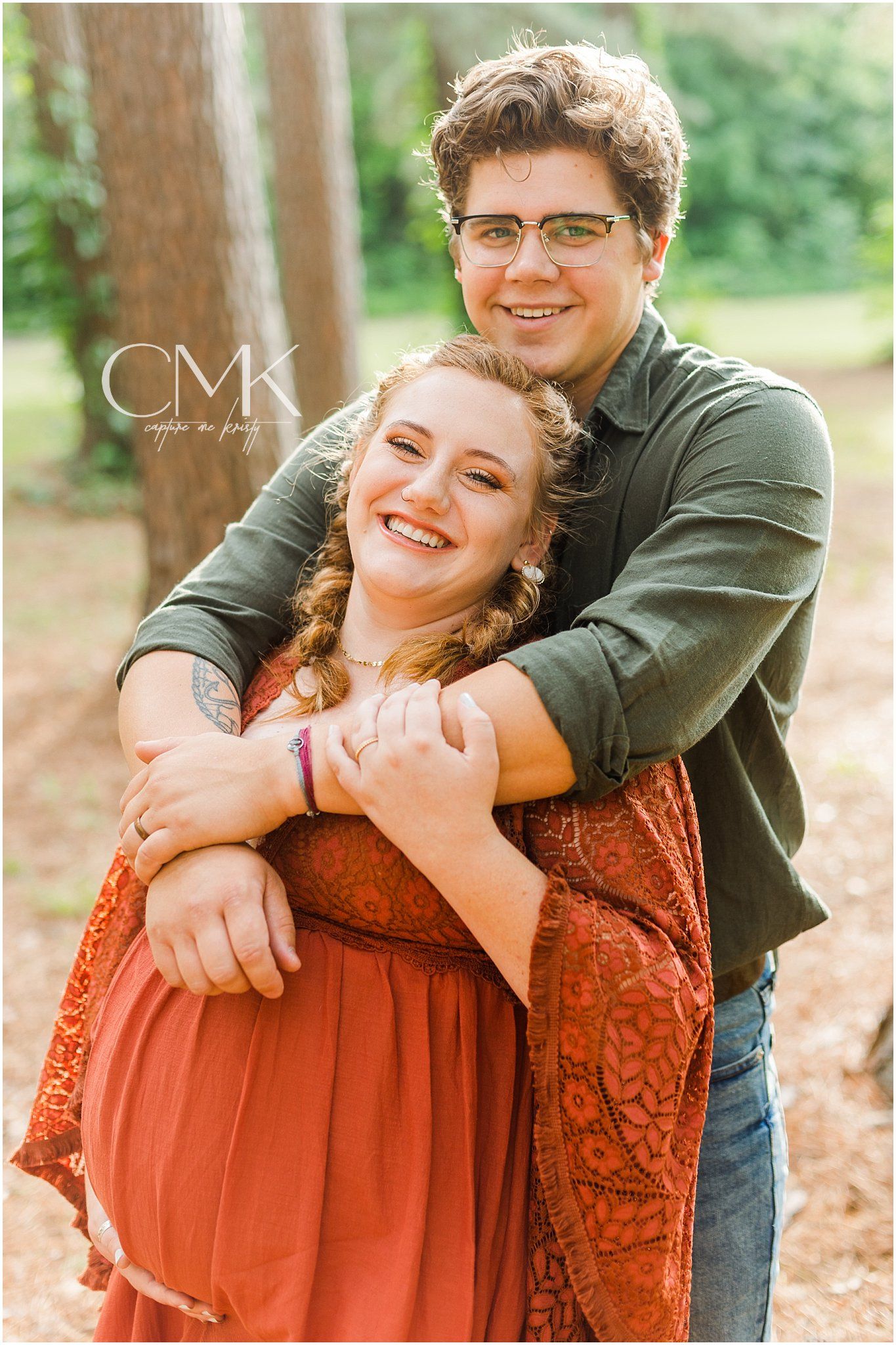 Joyful embrace during outdoor maternity photography session in wooded setting.