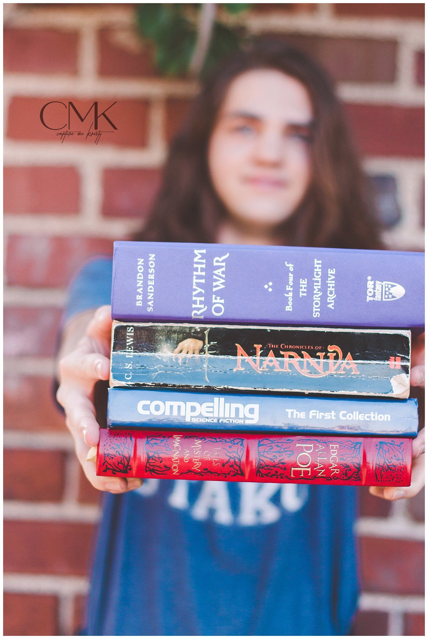 Person holding stack of books including Narnia against brick wall background.