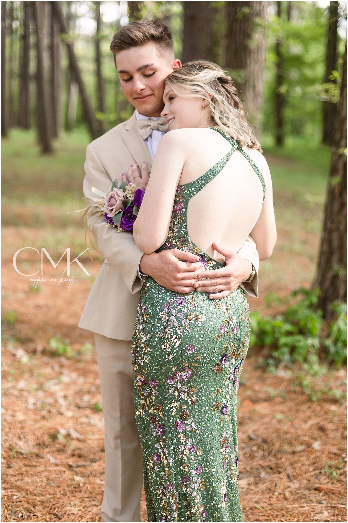 Formal couple sharing an intimate moment in a wooded setting with green sequined gown and beige suit.