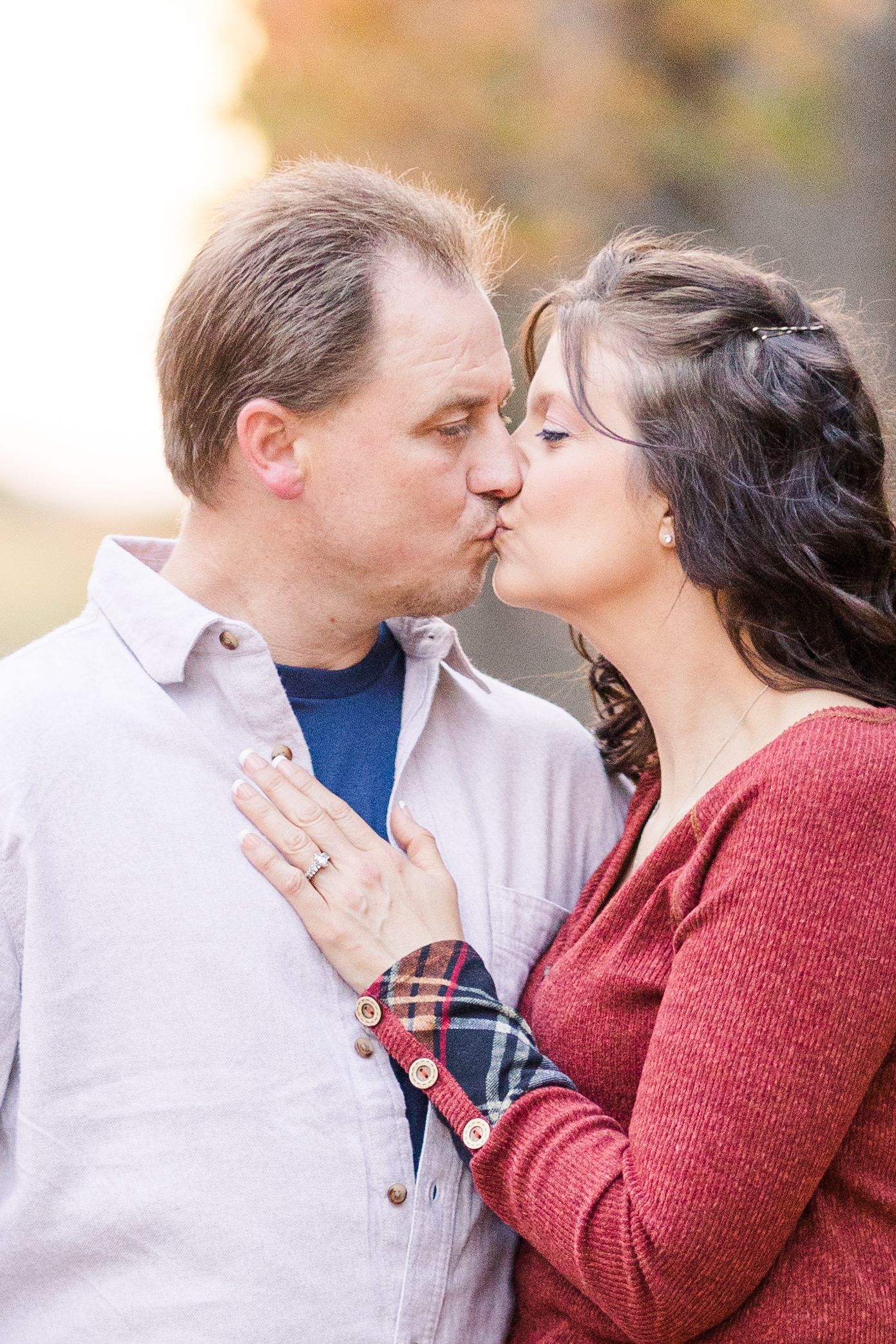 Romantic kiss captured during fall engagement photo session outdoors.