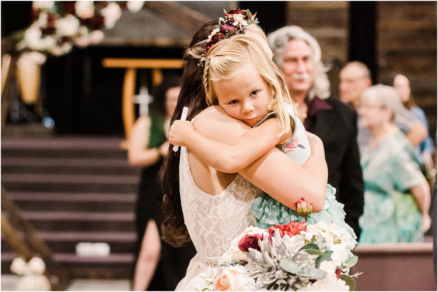 Close-up of a joyful embrace at a wedding ceremony with guests looking on in background.