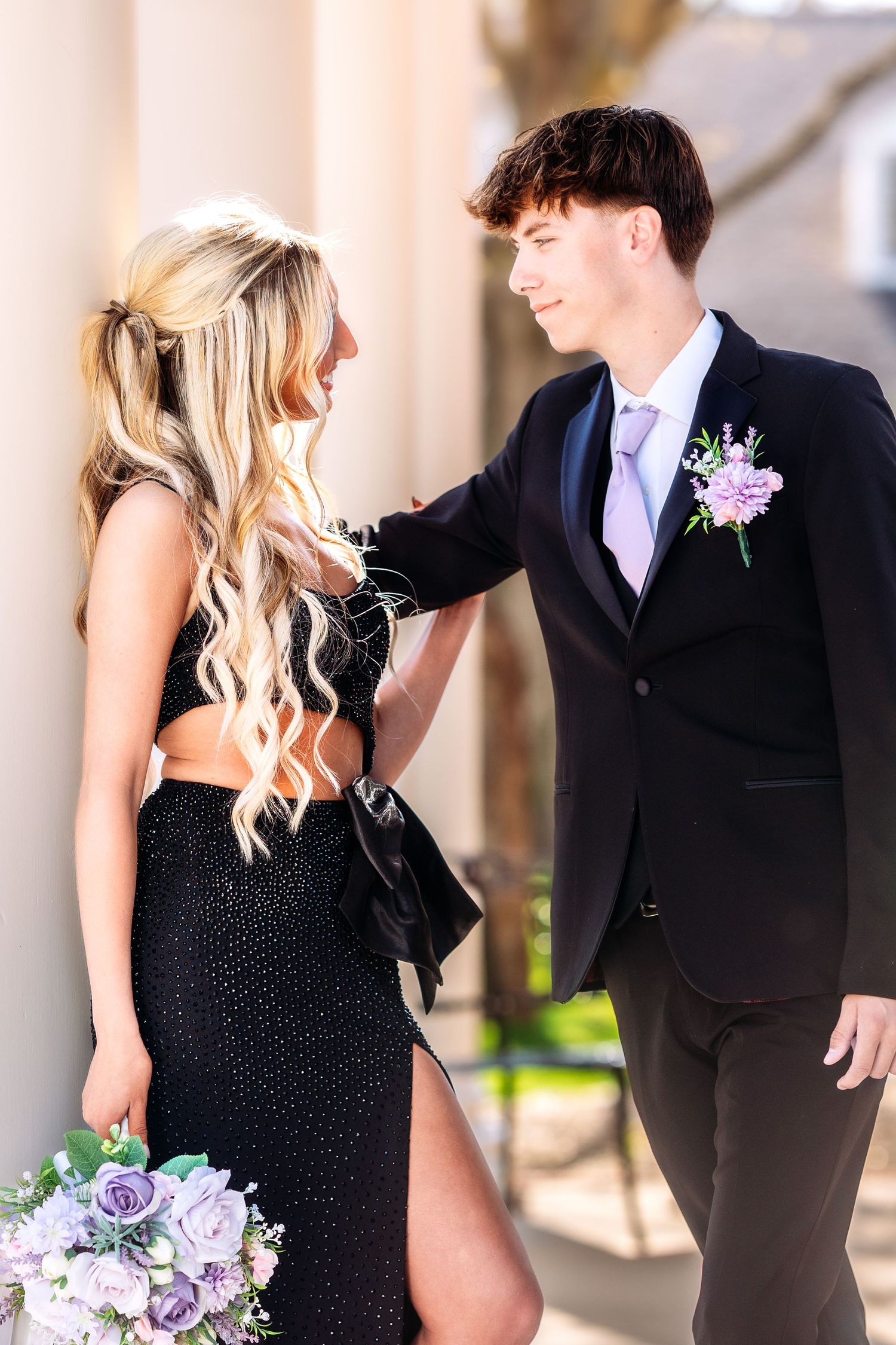 A couple in formal attire, with a black dress and suit, share candid moments during a wedding photo session.