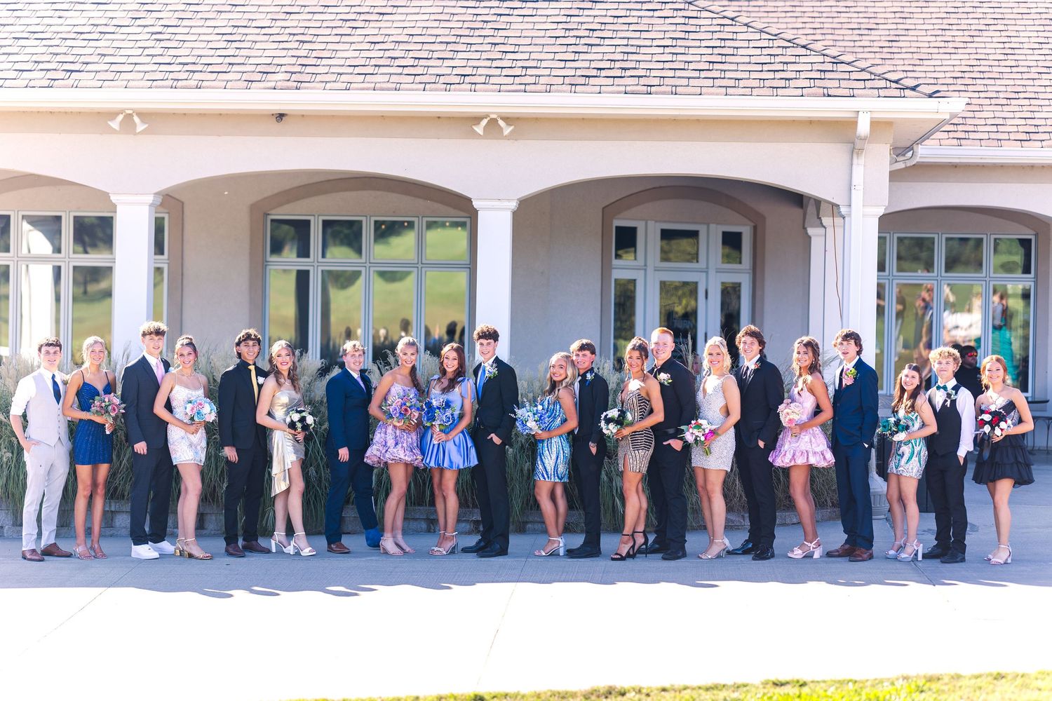 Large formal group photo of couples in suits and dresses lined up outside a building.