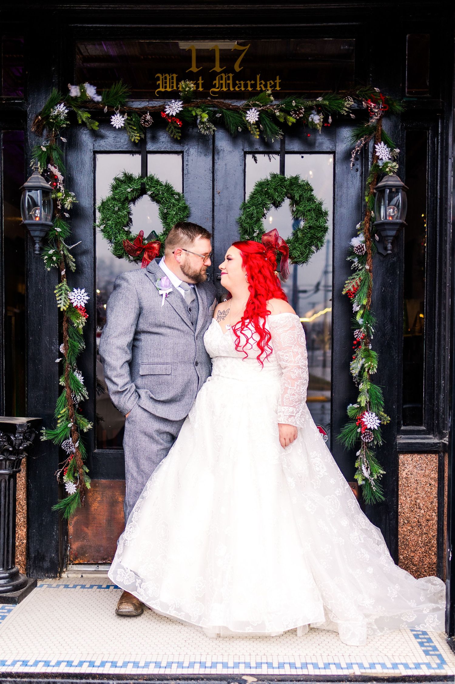 Wedding couple posing against storefront decorated with holiday wreaths and garland.