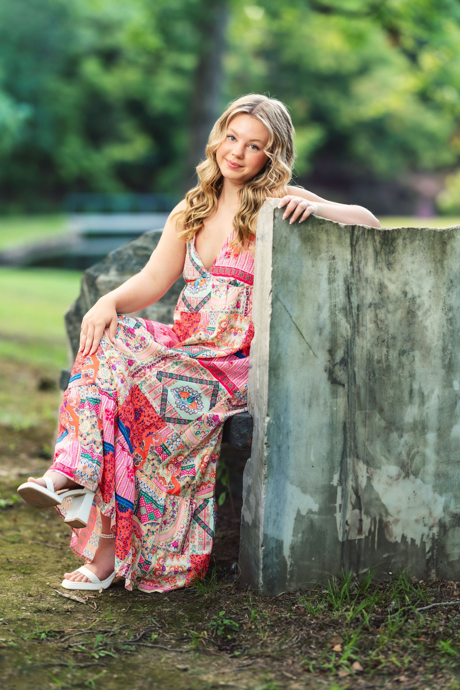 Person in colorful floral dress poses near concrete wall in outdoor garden setting.