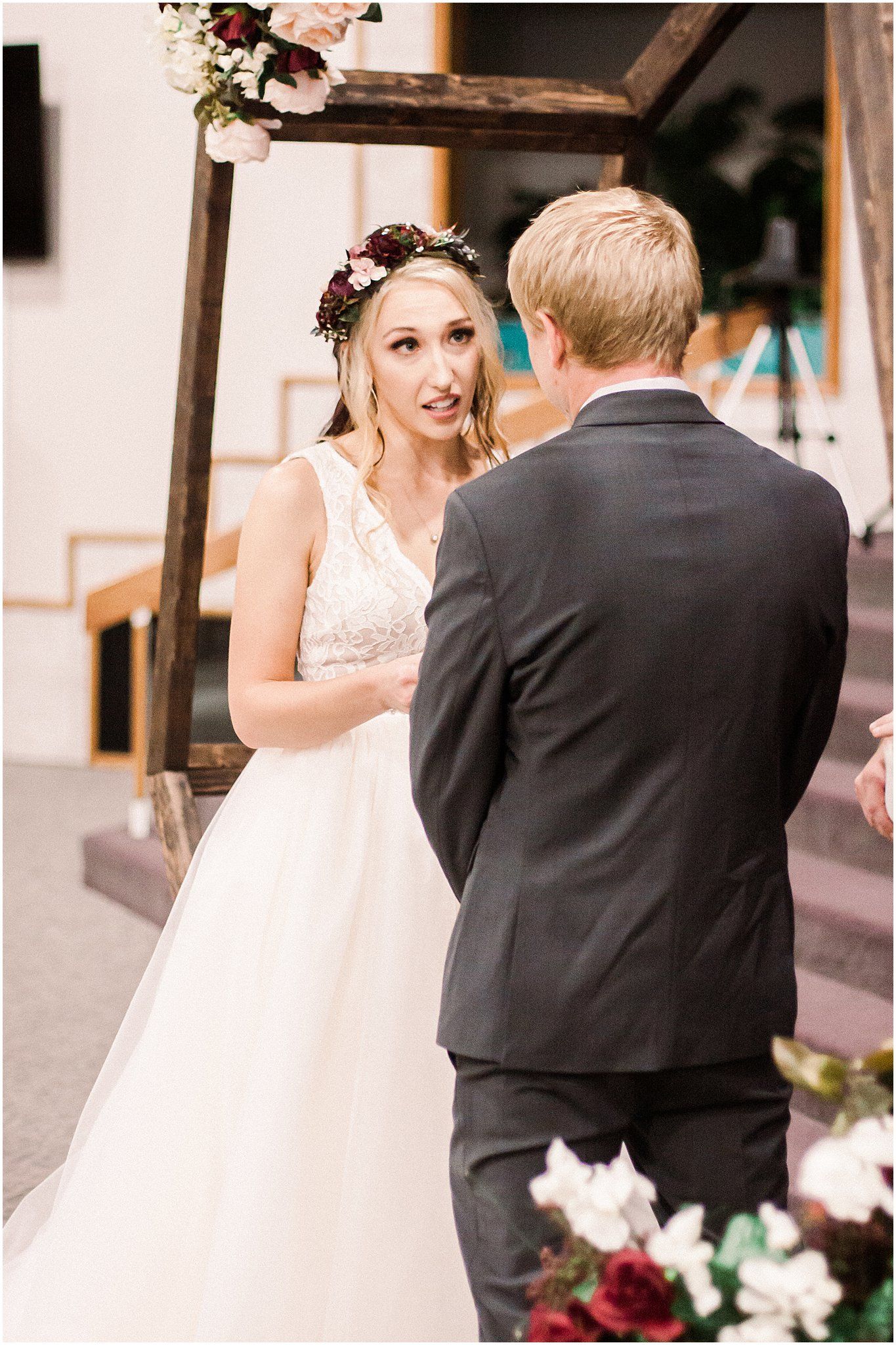 A bride in a lace dress and floral crown exchanges emotional vows during an indoor ceremony.