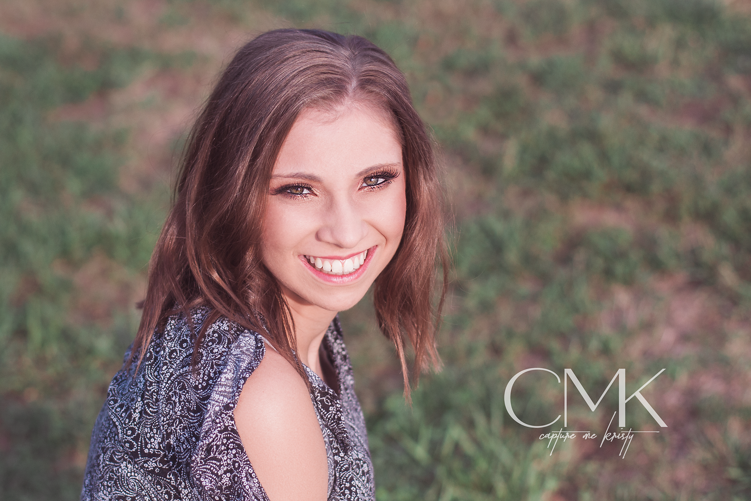 Natural light portrait with soft smile against blurred green background with CMK logo.