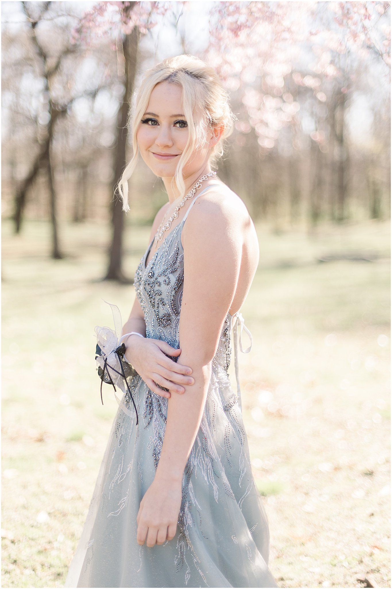 A person in a silver beaded formal gown poses in a sunlit outdoor setting.