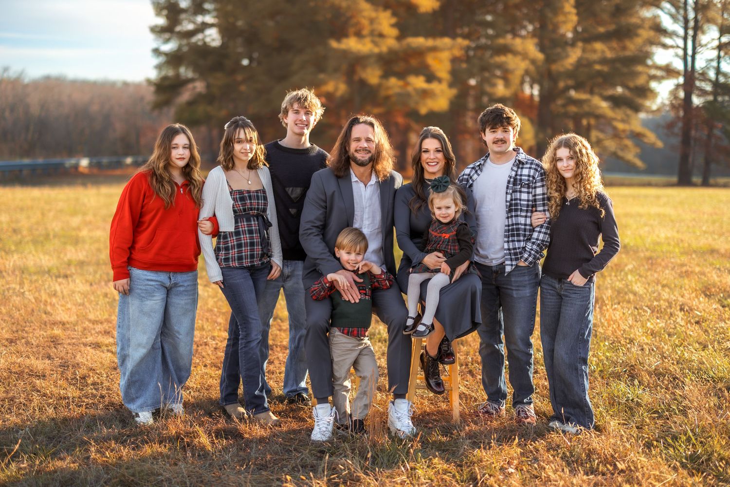 Extended family portrait session in casual wear during golden hour in an autumn field.