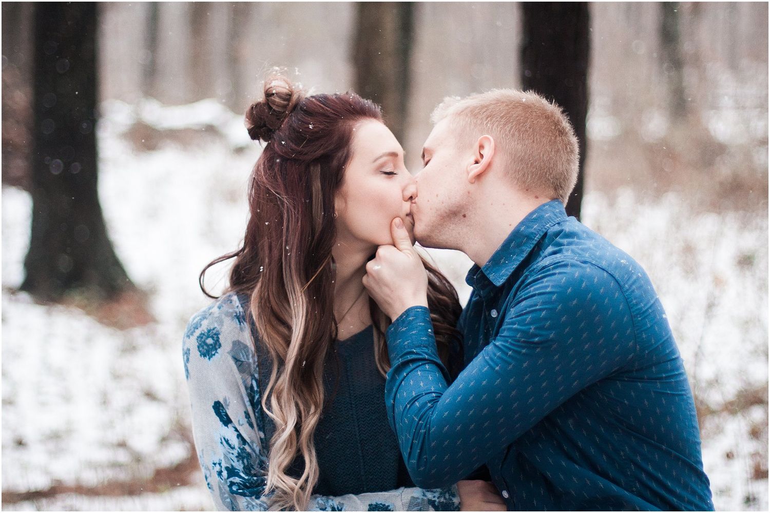 Couple sharing a tender winter kiss in the snow while wearing coordinated outfits.