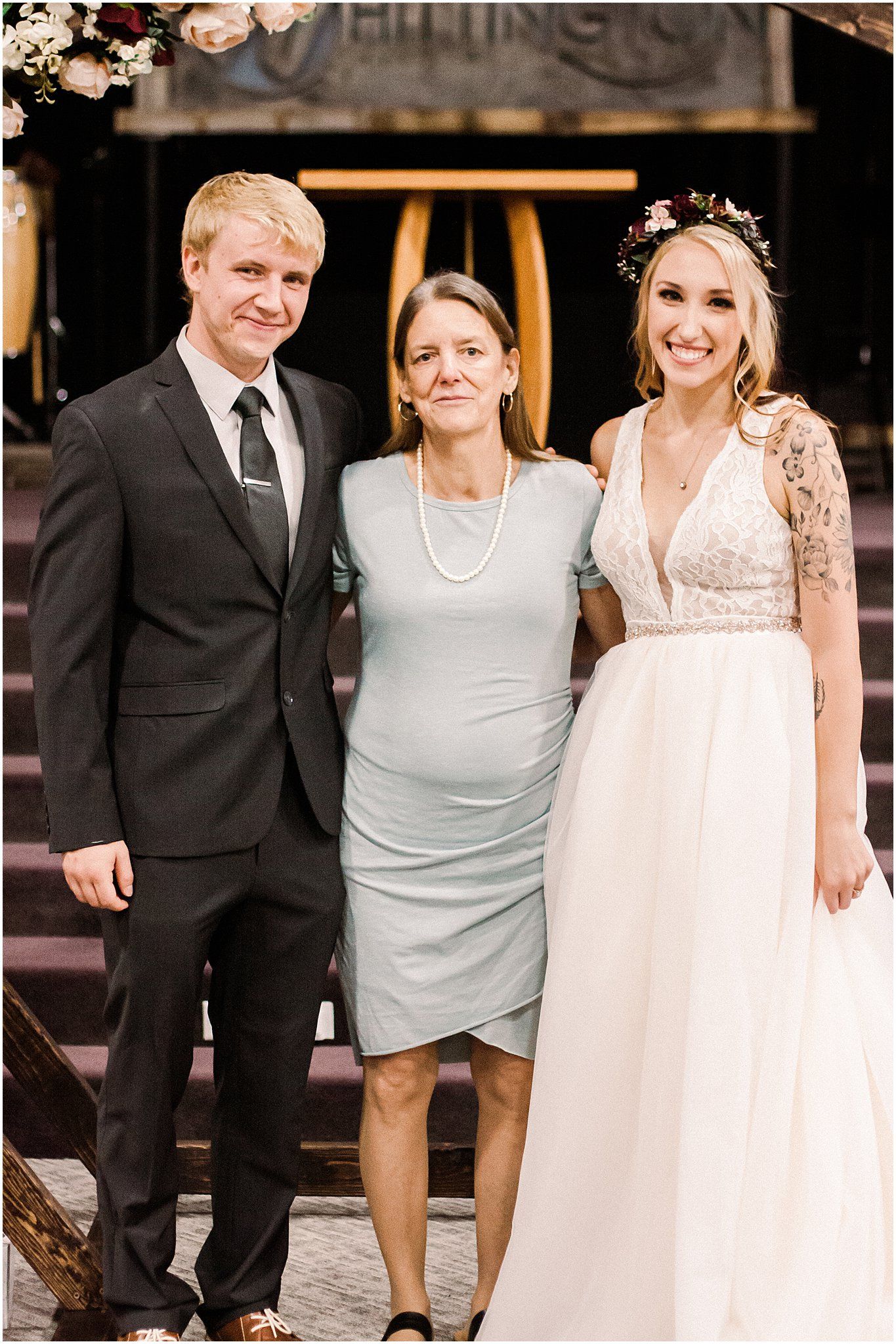 Three people pose formally at a rustic wedding venue with floral accents.