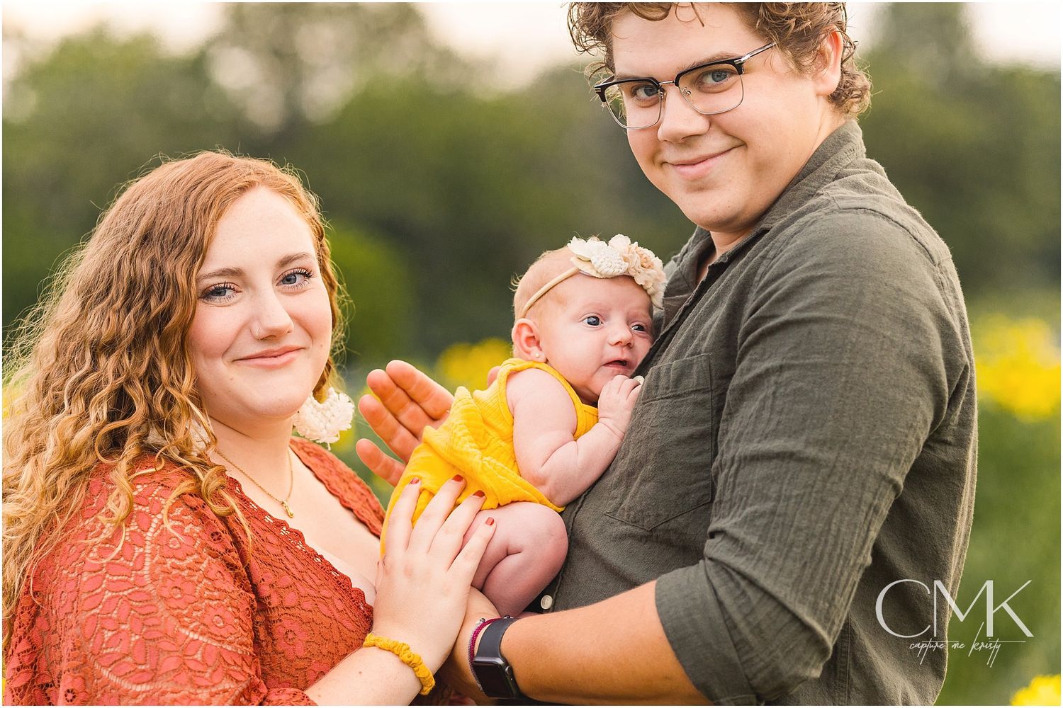 Family portrait in a flowery meadow with baby wearing bright yellow outfit.