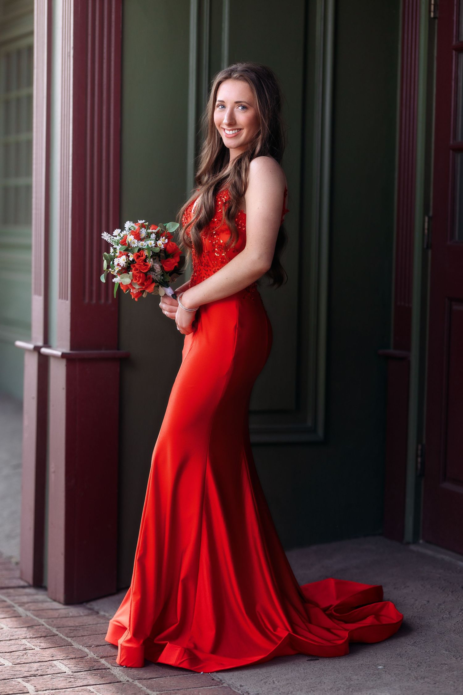 Flowing red formal gown with train photographed in elegant architectural setting.