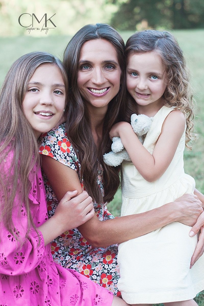 Three people smiling together in summer dresses during outdoor family photoshoot.