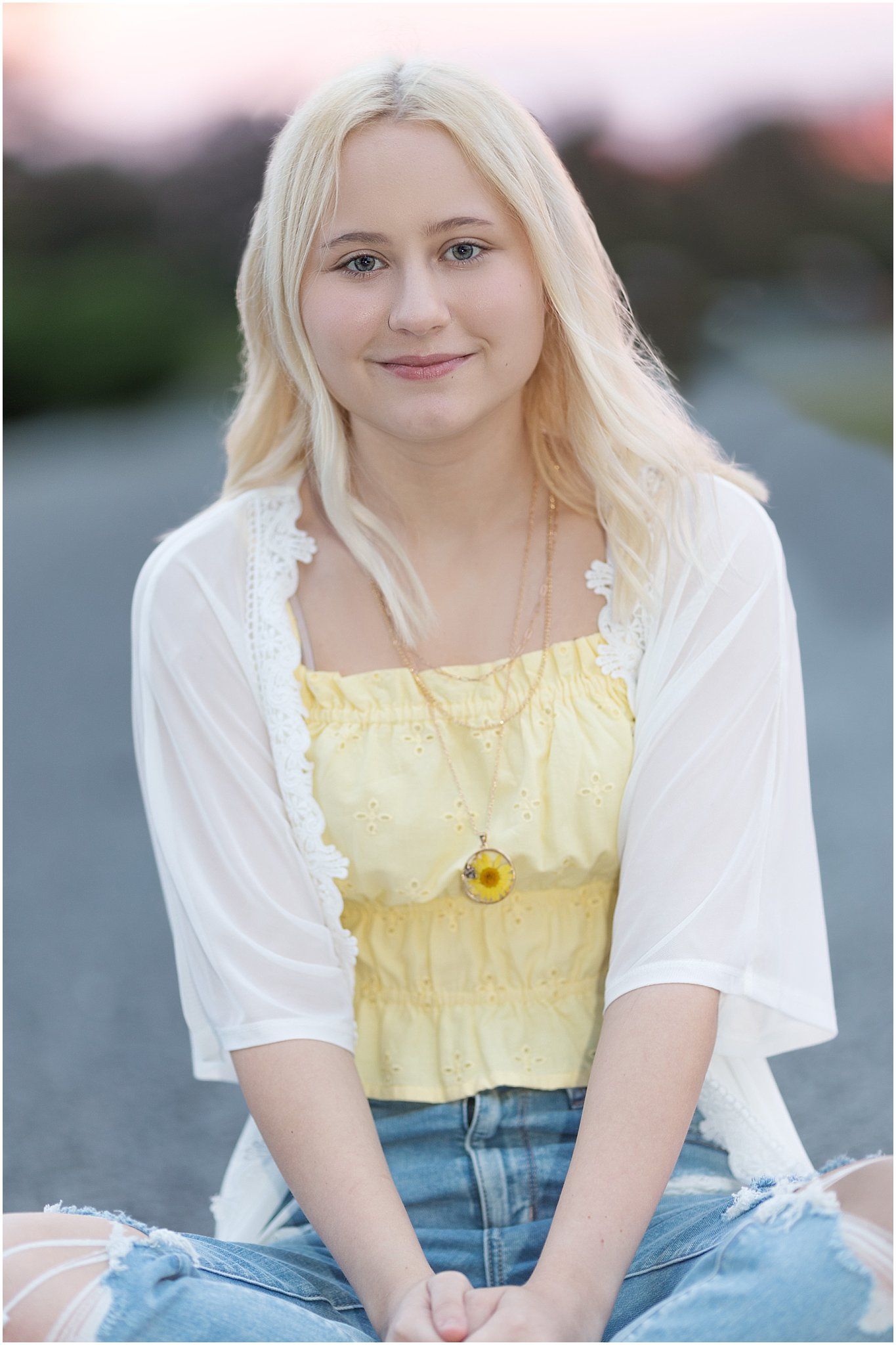 Senior girl sitting cross legged in road at sunset