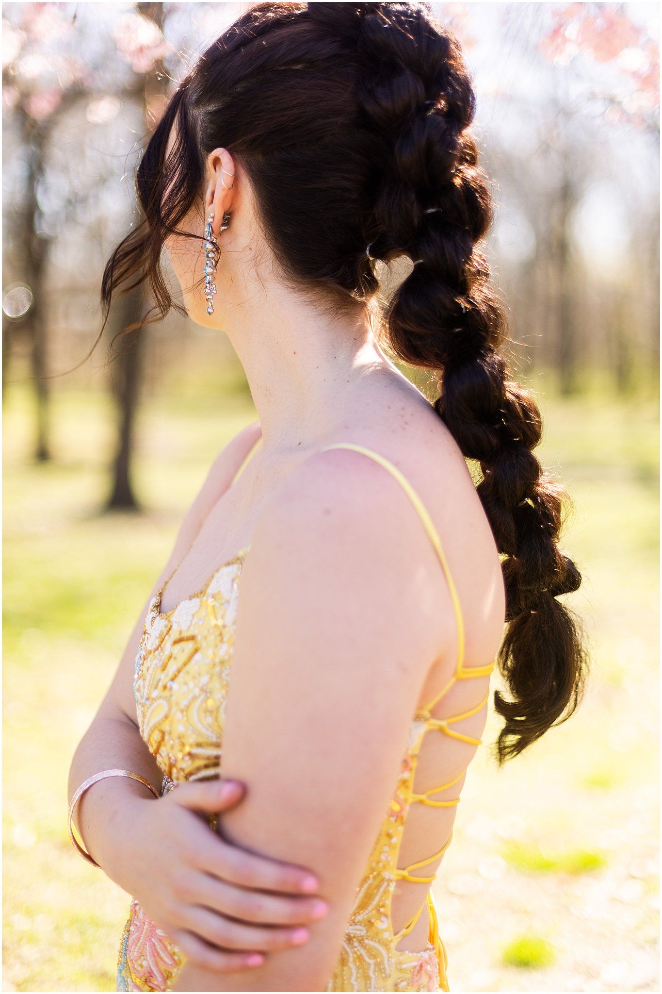 Elegant braided hairstyle with dangling earring shown from behind in yellow formal dress.