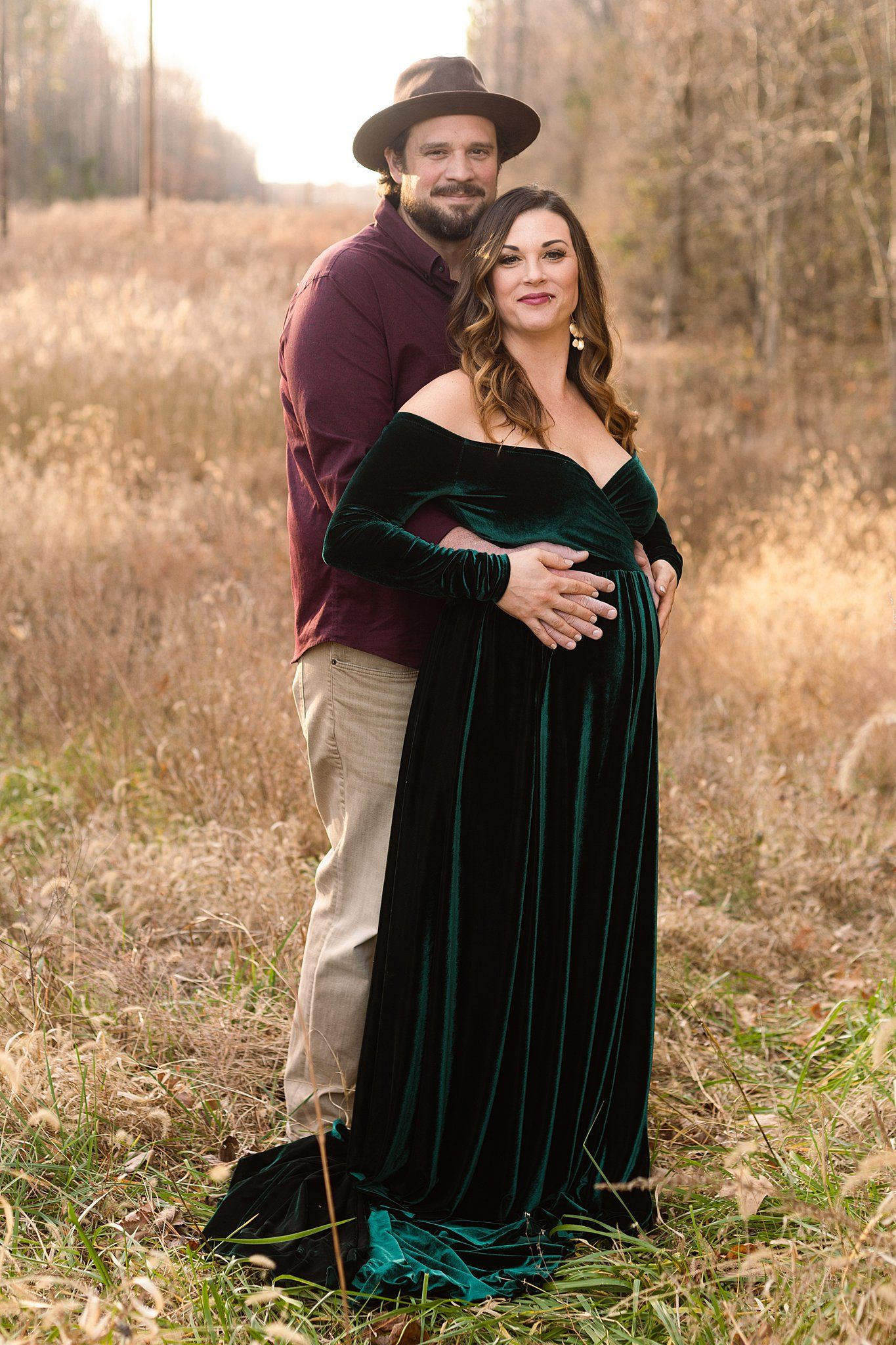 Romantic outdoor maternity photo with a couple in burgundy and emerald velvet against fall foliage.
