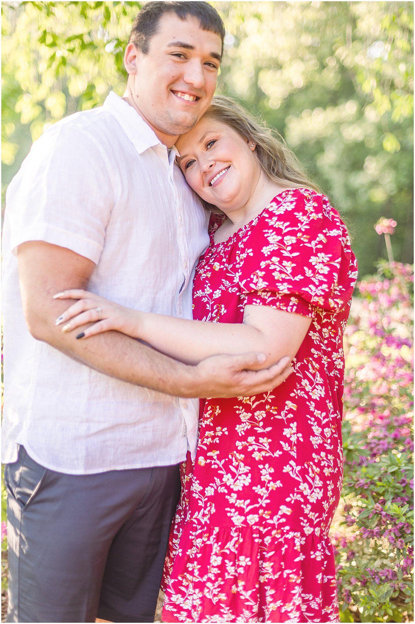Happy couple embraces while smiling in a garden setting with blooming flowers in background.