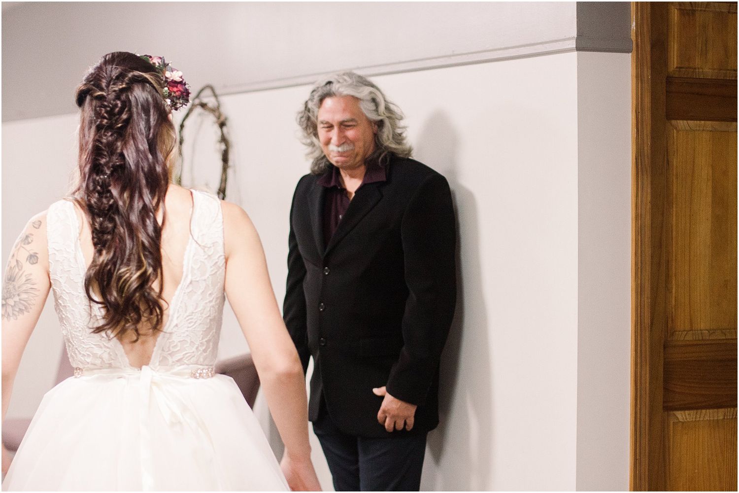 An emotional reveal between a bride in white lace and someone wearing black in a hallway setting.
