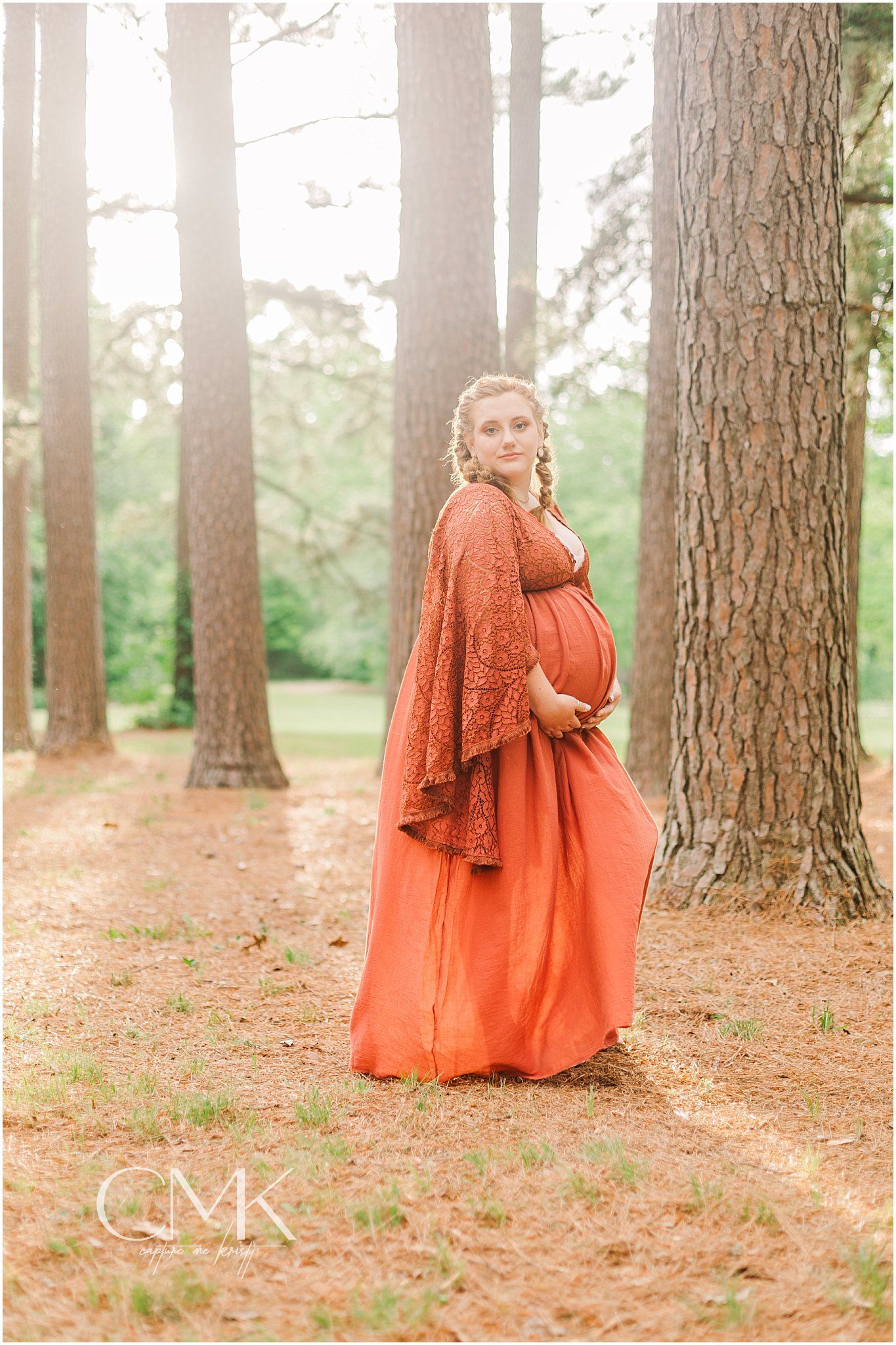 Outdoor maternity portrait featuring a flowing rust-colored dress against tall pine trees.