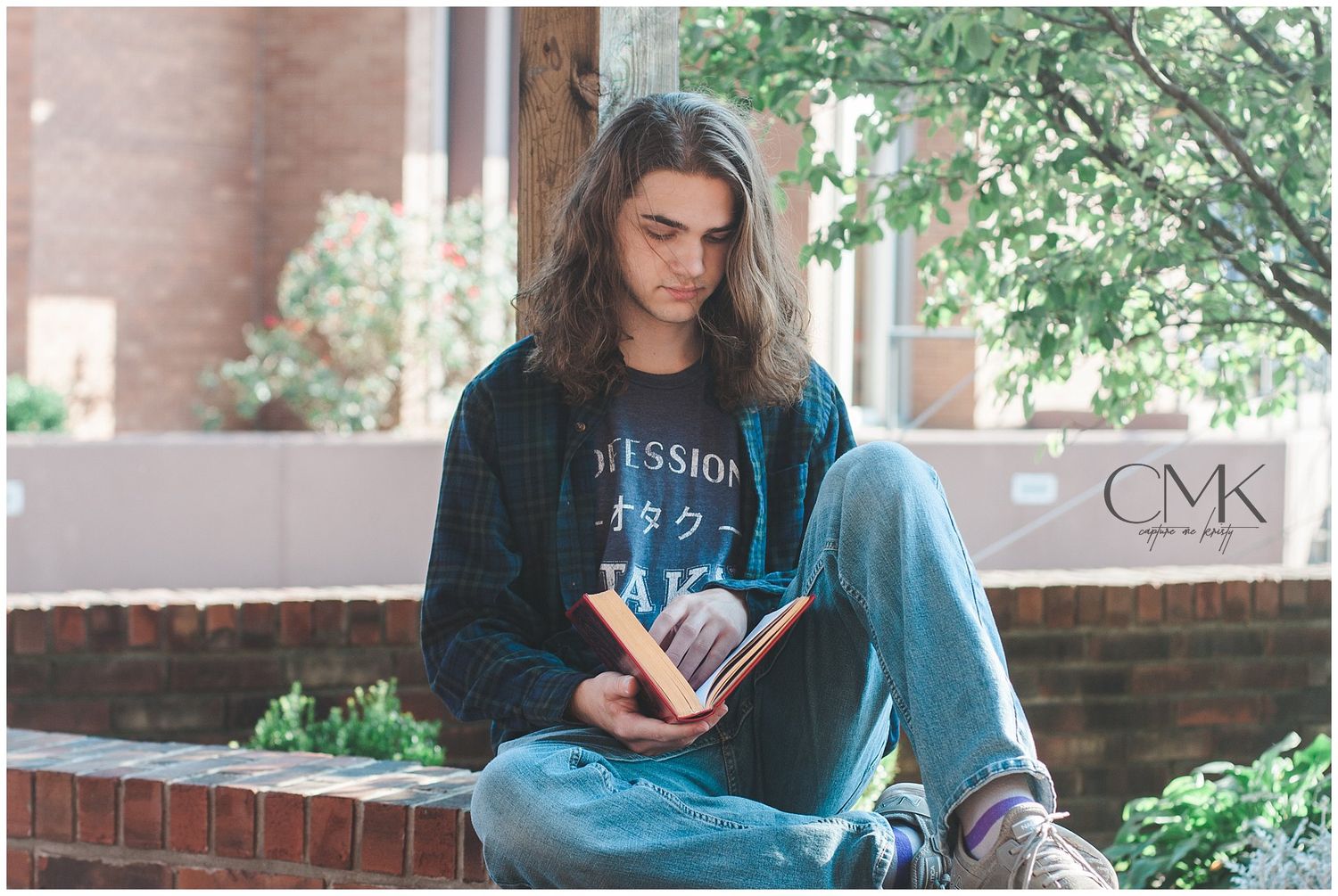 A person in denim and dark sweater reading while sitting on brick steps outdoors.
