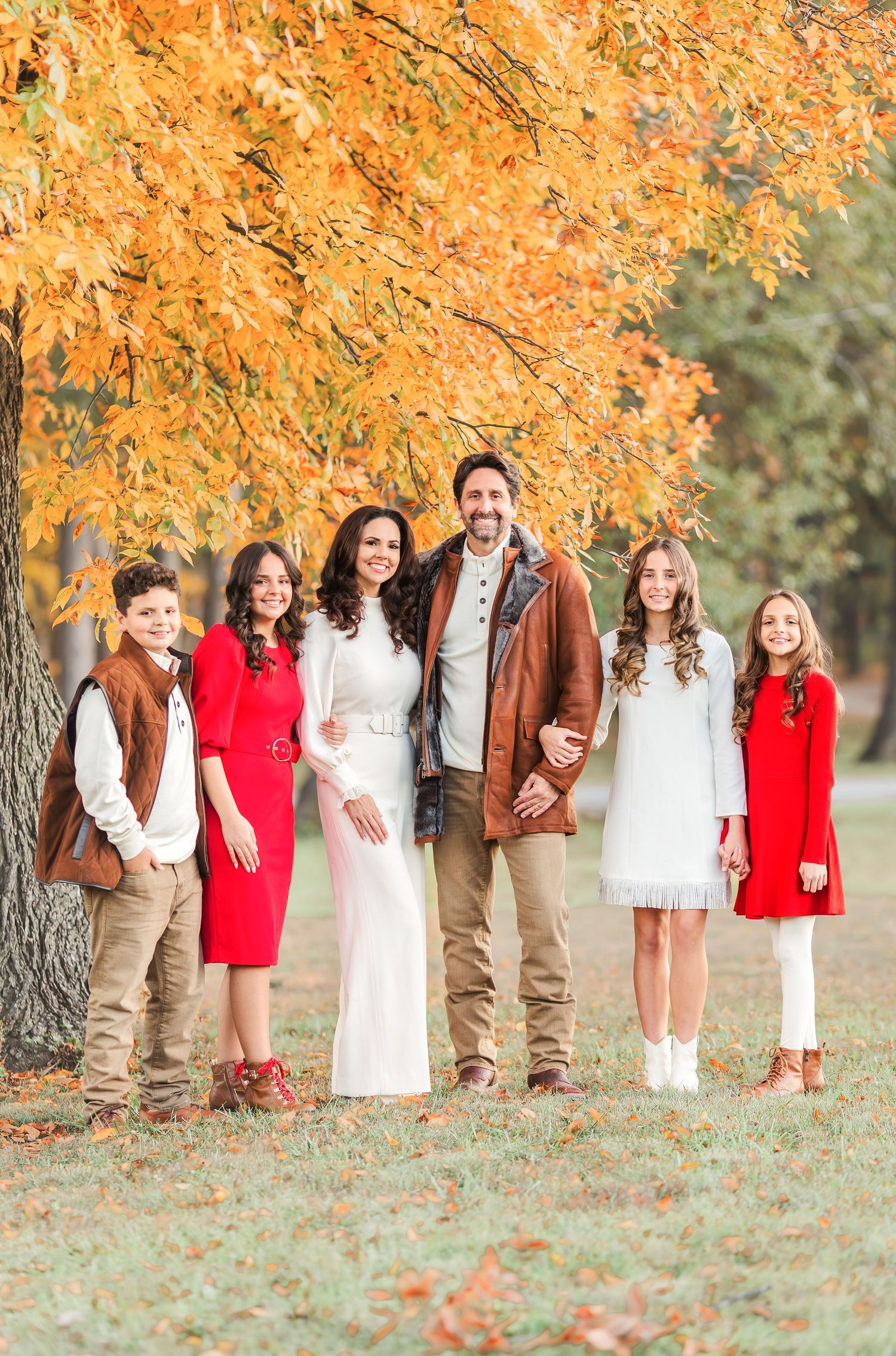 A group poses under vibrant orange fall foliage wearing coordinated red and white outfits.