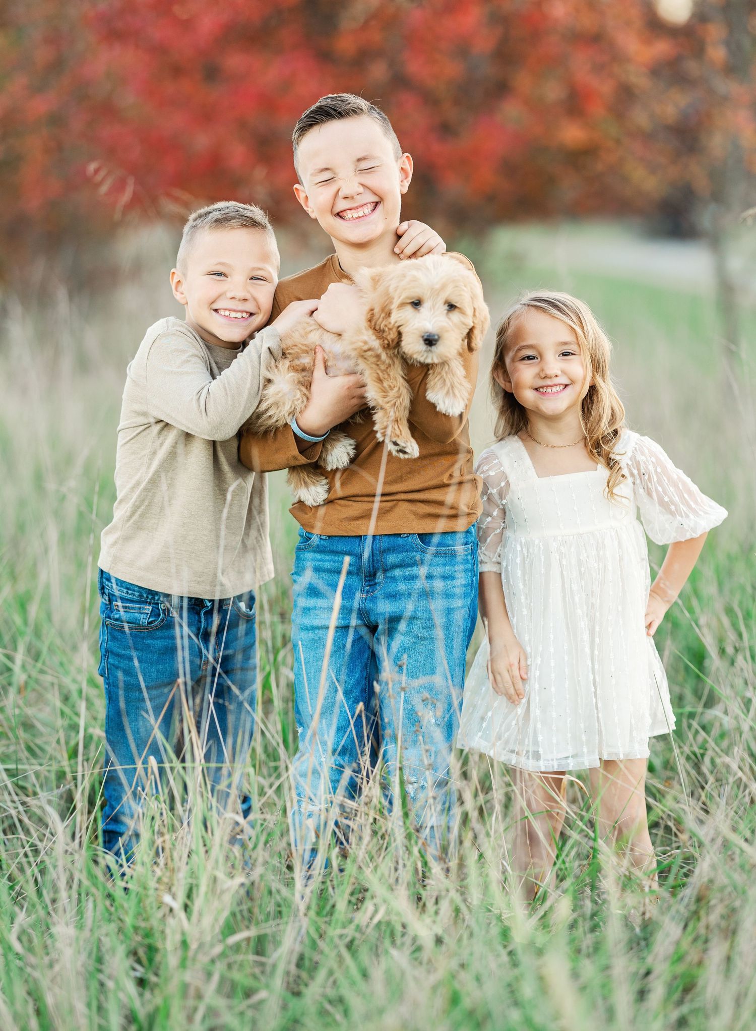 Happy family with golden retriever puppy stands together in tall grass.